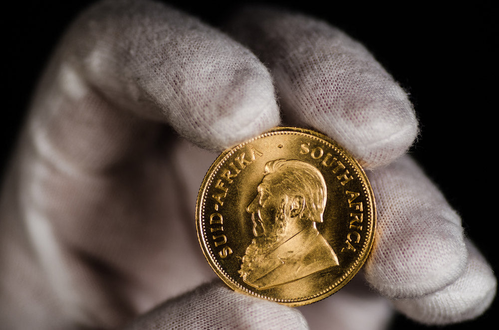 A gold Krugerrand held carefully in a white glove